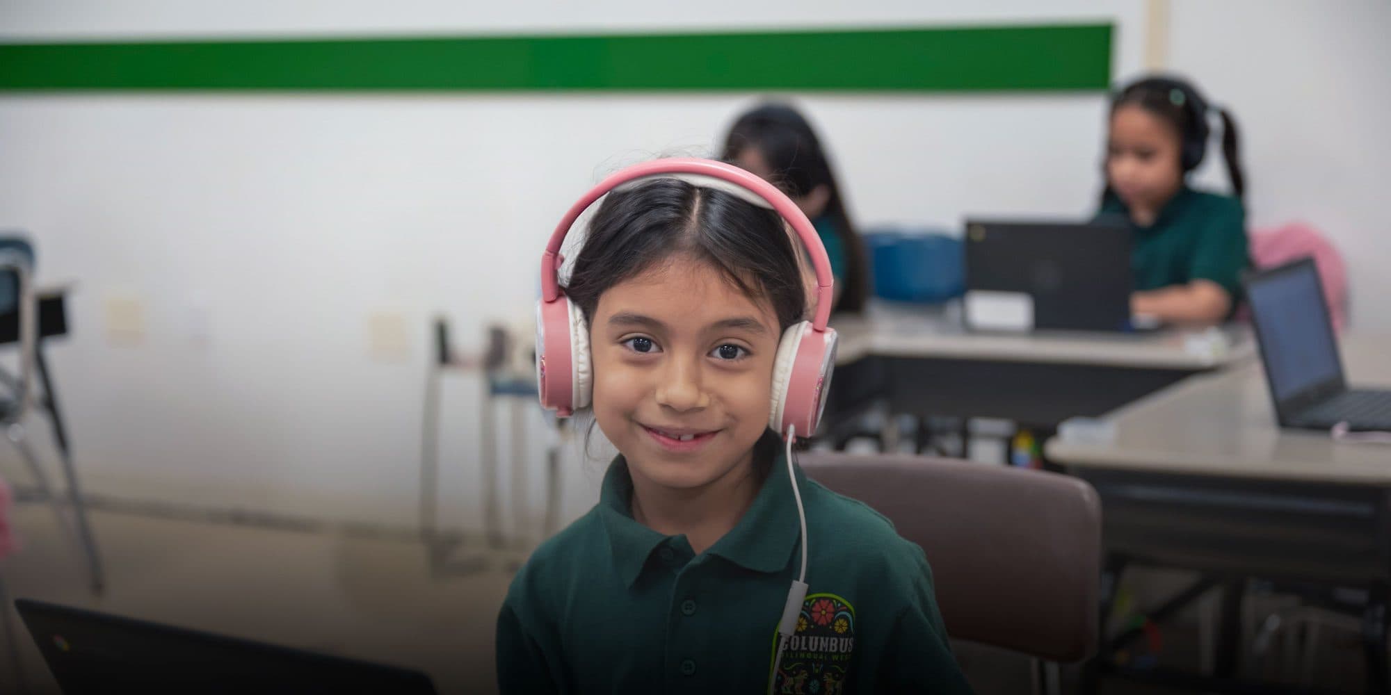 Smiling student wearing pink headphones in a Columbus Bilingual West classroom.